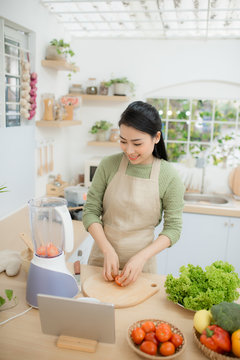 Image of young lady standing in kitchen using tablet computer and cooking vegetable salad