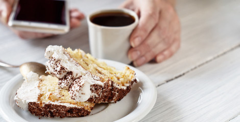 Tiramisu dessert and female hands with smartphone and cup of coffee