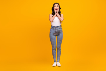 Full length photo of pretty cheerful lady good mood slim figure shapes energetic person arms on cheeks wear white tank-top jeans footwear isolated bright yellow color background