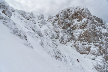 Two climbers under the steep winter slope of a mountain plateau in Crimea