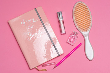 Naklejka premium pink notebook, lip gloss, perfume probe and plastic comb on a pink background