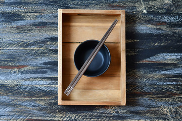  A bowl & brown chopsticks on it on a tea tray on a multi-colored dark surface