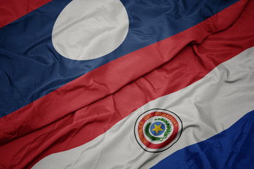 waving colorful flag of paraguay and national flag of laos.