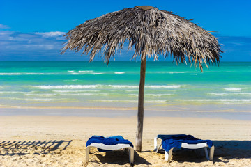 Waiting for the vacation. Vacation in Cuba. Beach holiday. Vacation on the Caribbean coast. Sun beds and an umbrella made of palm leaves on the background of emerald water. An invitation to rest.