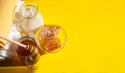 Natural home skin care. The pleasure of taking a bath. Sweet Golden honey, milk and clean towels on a yellow background. The soft sunlight. Free space.