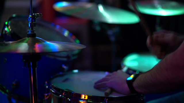 A male drummer sits behind a drum kit and beats drumsticks on drums and cymbals. Slow motion, close-up, artificial lighting in a night club