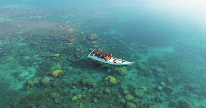 Beautiful 4K UHD aerial drone shot of a fishing boat in a tropical Pacific paradise diving coral reef around islands in Indonesia / Thailand / Asia, with clear blue water, corals and sandy beaches.
