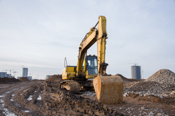 Obraz premium Excavator working at construction site. Backhoe digs ground for the foundation and for paving out sewer line. Construction machinery for excavating, loading, lifting and hauling of cargo on job sites
