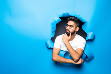 Young handsome indian bearded man thinking look from blue paper hole