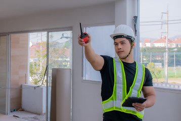 Strong foreman wearing a white helmet, holding a radio communication and a tablet on the...