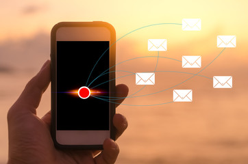 Man hand using smartphone at sunset beach with email icon background. Technology business and travel freedom concept.