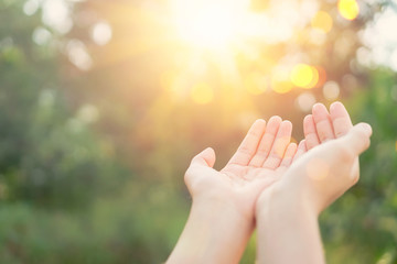 Woman open hand up to sunset sky and green blur leaf bokeh sun light abstract background.