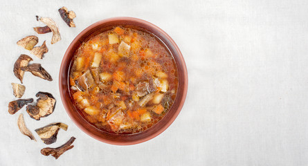 Wild mushroom mushroom soup in a brown clay plate on linen cloth, top view, copy space