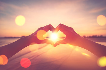 Female hands heart shape on nature bokeh sun light flare wave and blur tropical beach abstract...