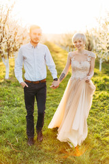 Fototapeta na wymiar Smiling couple in love having amazing walk in blossoming tree garden. Elegant couple walks through a blooming garden in the spring, holding hands and looking at camera