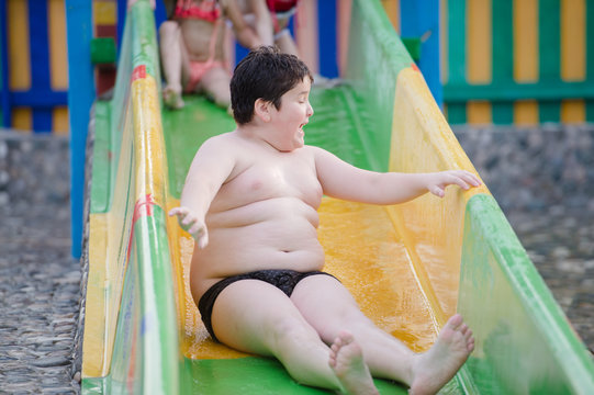 funny little fat thick boy on water slide during summer leisure activity