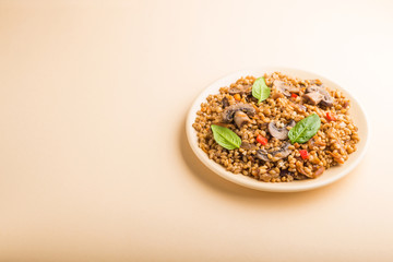 Spelt (dinkel wheat) porridge with vegetables and mushrooms on ceramic plate on orange background. Side view, copy space.