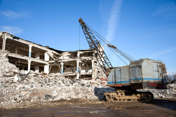 Crawler crane with a heavy metal wrecking ball on a steel cable at demolition of tall building....