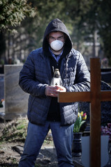 Man stands over the grave of a deceased coronavirus in the cemetery, wearing a protective mask.
