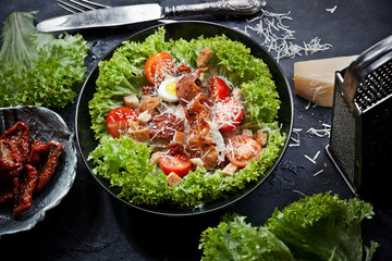 kitchen table with green salad, bowls with tomatoes, parmesan cheese and grater, fork and knife, flatlay