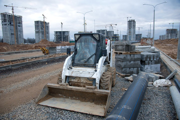 Bobcat skid-steer loader for loading and unloading works on city streets. Сompact construction equipment for work in limited conditions. Road repair at construction site. 