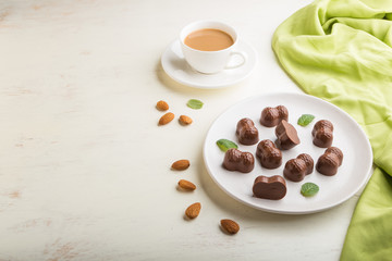 Chocolate candies with almonds and a cup of coffee on a white wooden background. side view, copy space