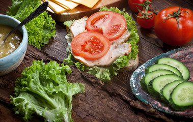 meat sandwich with fresh tomatoes, green salad, cucumbers, cheese and sauce on dark wooden table background