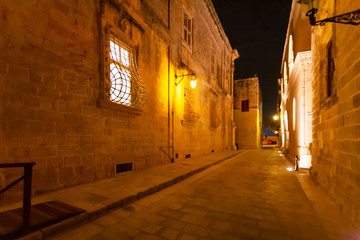 Narrow streets of Mdina, ancient capital of Malta. Night view on illuminated buildings and wall decorations of ancient town.