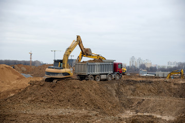 Excavator load the sand to the heavy dump truck on construction site. Backhoe at earthworks. Digs a pit for the construction of the road. Digging trench for laying sewer pipes drainage in ground.