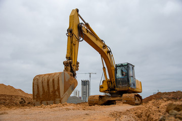 Excavator at earthworks on construction site. Backhoe loader digs a pit for the construction of the foundation. Digging trench for laying sewer pipes drainage in ground. Earth-Moving Heavy Equipment
