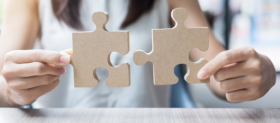 woman hands connecting couple puzzle over table, businesswoman holding wood jigsaw inside office. Business solutions, mission, target, success, goals and strategy concepts - obrazy, fototapety, plakaty