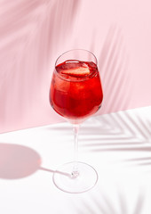 Red summer cocktail with strawberry in wine glass on creative background
