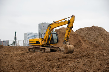 Excavator working at construction site on earthworks. Backhoe digs ground for the foundation and for paving out sewer line. Construction machinery for excavating, loading, lifting and hauling of cargo