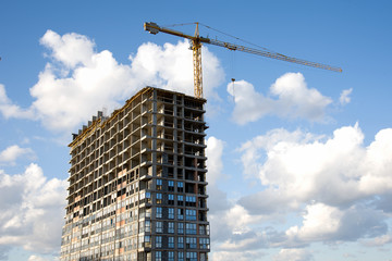 Fototapeta na wymiar Tower crane working at construction site on blue sky background with white clouds. Construction process of the new residential buildings. Installing double glazed windows