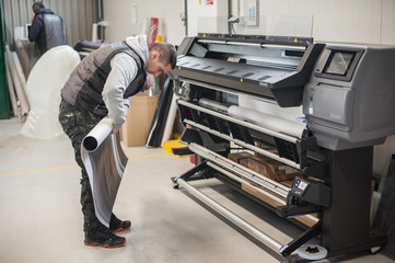 Technician operator changes paper roll on large printer plotter machine