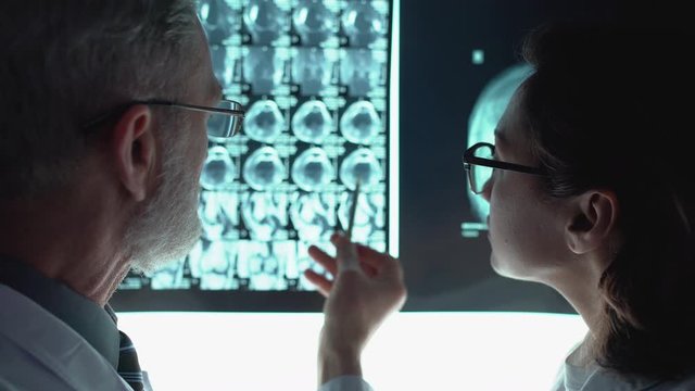 Two doctors in eyeglasses discussing diagnosis, analyzing tomographic picture