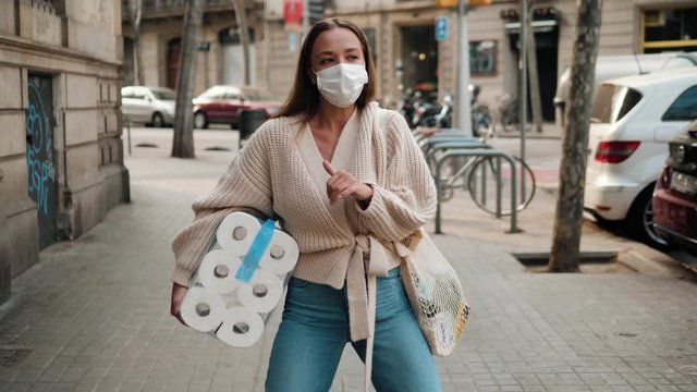 Woman happy dancing in medical mask with toilet paper and packs of pasta food shopping bags during the quarantine coronavirus COVID-19 pandemic in 2019-2020