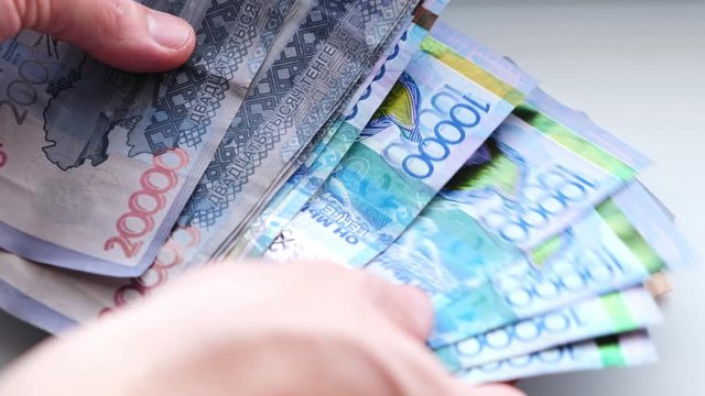Man recalculates banknotes of Republic of Kazakhstan tenge, five, ten twenty thousand denominations.