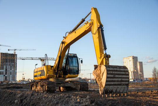 Track-type excavator during earthmoving at construction site. Backhoe digging the ground for the foundation and for laying sewer pipes district heating. Earth-moving heavy equipment