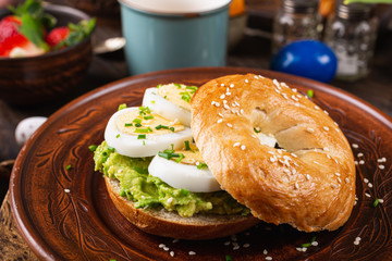Healthy freshly baked bagel filled with boild eggs, avocado and chives. Breakfast food.