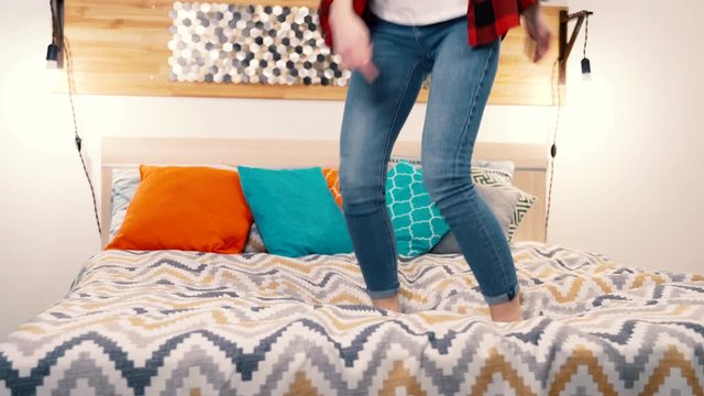 A young woman is having fun jumping on the big double bed in a hotel or a modern bedroom.