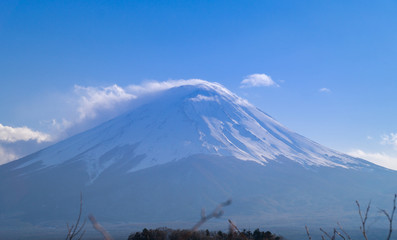 A beautiful full view of the fuji mountain with snow and clouds covering the top.