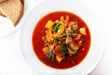 Hot beef hungarian  goulash soup with paprika, beef, potatoes, carrots, onion, pepper and herbs. White background. High key. Top view.