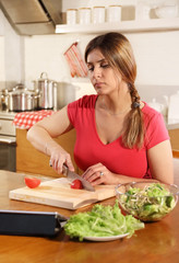 Attractive young adult woman prepares a salad using a digital tablet to read a recipe on the Internet