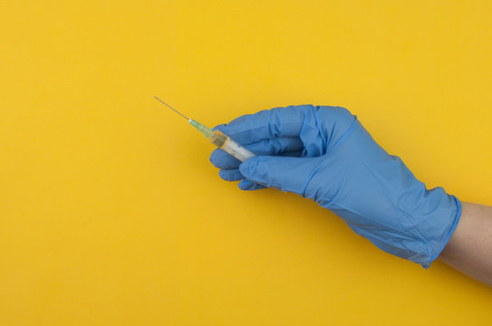 Doctor's hand in a blue rubber glove holds a medical syringe on a yellow background. The concept of medicine and medical care for the patient