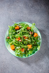 Delicious salad with arugula, baked pumpkin, hazelnut and sesame seeds on green plate. Paleo diet food concept. Top view.