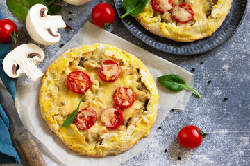 Homemade pastries with whole grain flour. Galette with chicken, cheese and mushrooms on a stone or slate countertop. Copy space.