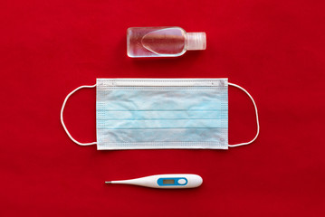 Protective face mask, antiseptic and thermometer on red background. Virus and disease protection...
