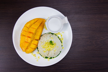 Sticky rice with fresh ripe mango with coconut milk put white plate on brown dark wooden table is thai style tropical dessert. Top view.