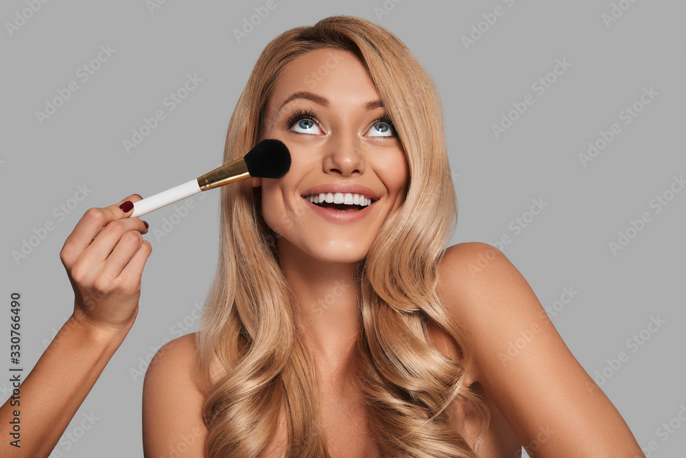 Wall mural attractive young woman with fresh glowing skin applying beauty product and smiling while standing ag